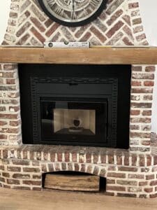 Insert de poêle à granulés Nobis noir dans âtre en briques rouges à chevrons, sous une horloge et une poutre en bois. Niveau à bulle visible.