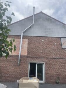 Gaine de cheminée métallique neuve installée sur une façade en briques rouges et bardage gris, avec un feuillage vert au premier plan.