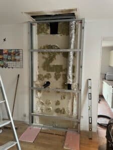 Structure métallique pour cloisonnement en cours, laissant voir isolation R48 et gaine d'aération. Niveau à bulle utilisé.