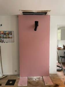 Plaque de plâtre rose (type ignifuge/humidité) installée en construction, avec une sortie de conduit noir traversant le milieu et un espace au plafond.