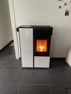 Poêle à granulés moderne blanc et noir allumé, créant une ambiance chaleureuse sur un sol carrelé foncé.