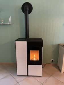 Poêle à granulés moderne, noir et blanc, avec flamme visible, raccordé à un conduit d'évacuation noir, dans un intérieur aux murs vert d'eau.