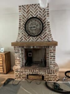 Cheminée rustique en briques rouges à chevrons avec horloge squelette, en cours de rénovation avec outils Makita et protection au sol.