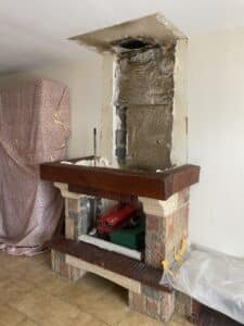 Cheminée ancienne en cours de rénovation, foyer ouvert, manteau en bois massif, conduit endommagé partiellement isolé d'une feuille argentée.