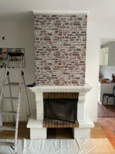 Cheminée avec hotte recouverte d'un papier peint imitation brique rouge vieillie, échelle à côté, préparatifs de rénovation.