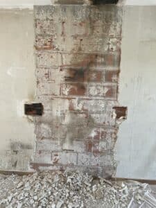 Mur en briques creuses exposé après retrait du plâtre ; débris de construction au sol ; inscriptions murales "22" et "213".