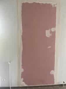 Mur bleu clair en rénovation avec une ouverture rectangulaire bâchée en plaques de plâtre rose et enduit de joint blanc.