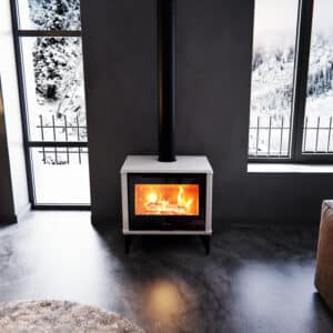Poêle JOLLY MEC blanc, design moderne, avec feu ardent et conduit noir. Intérieur gris minimaliste face à une double vue hivernale enneigée.