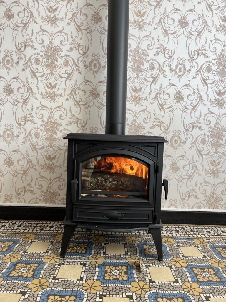 Poêle à bois noir en fonte avec feu de bûches flamboyant sur sol en mosaïque et papier peint damassé élégant.