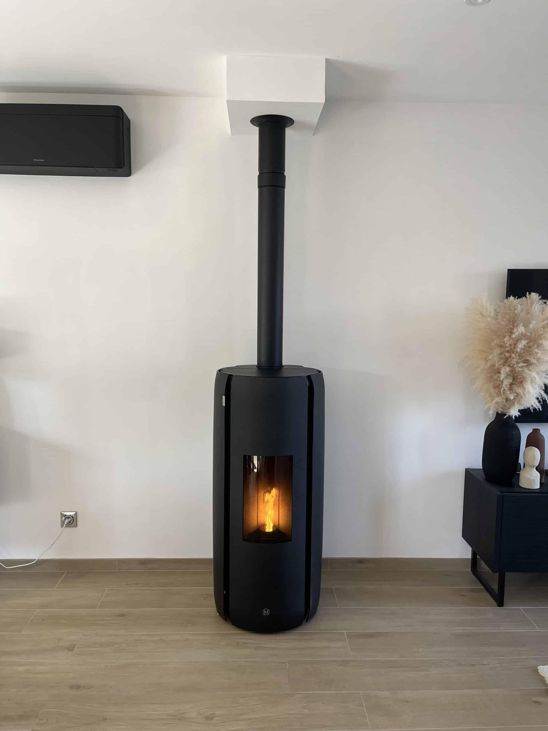 Poêle à granulés design noir pour un salon moderne Poêle à granulés cylindrique noir moderne allumé dans un intérieur minimaliste blanc et bois.