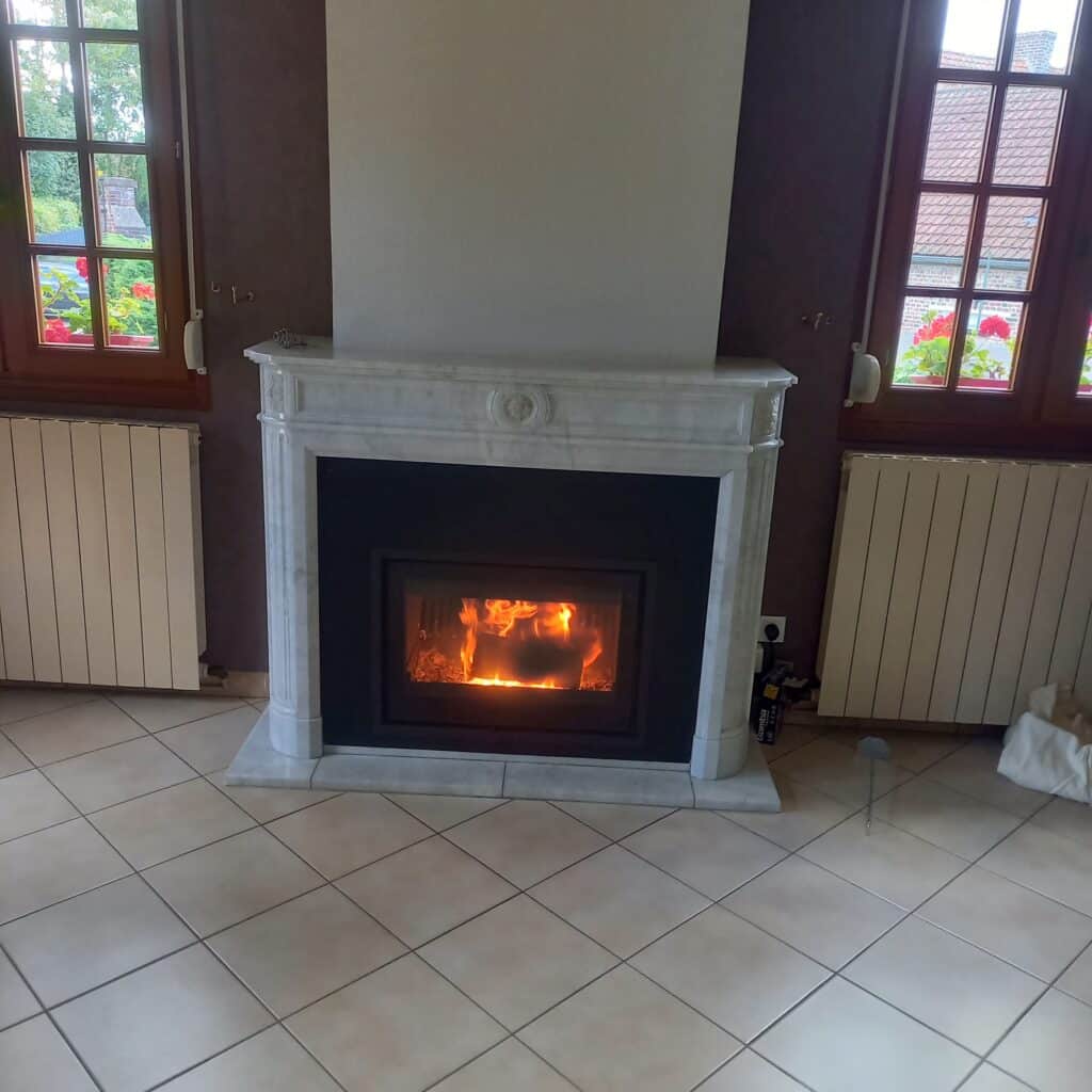 Cheminée en marbre blanc avec feu de bois, salon aux murs violets, grandes fenêtres et radiateurs.