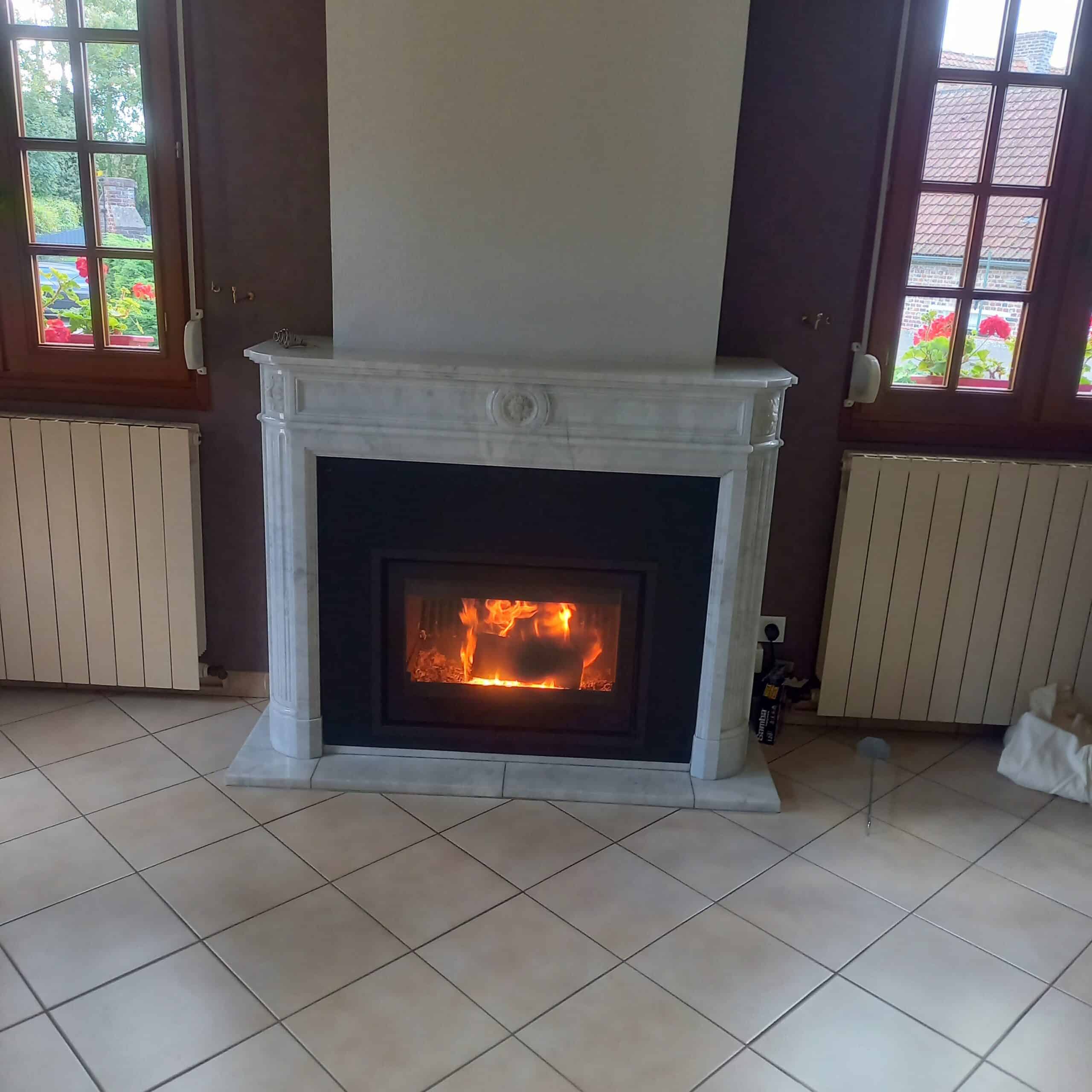 Cheminée en marbre blanc et insert bois chaleureux Cheminée en marbre blanc avec feu de bois, salon aux murs violets, grandes fenêtres et radiateurs.