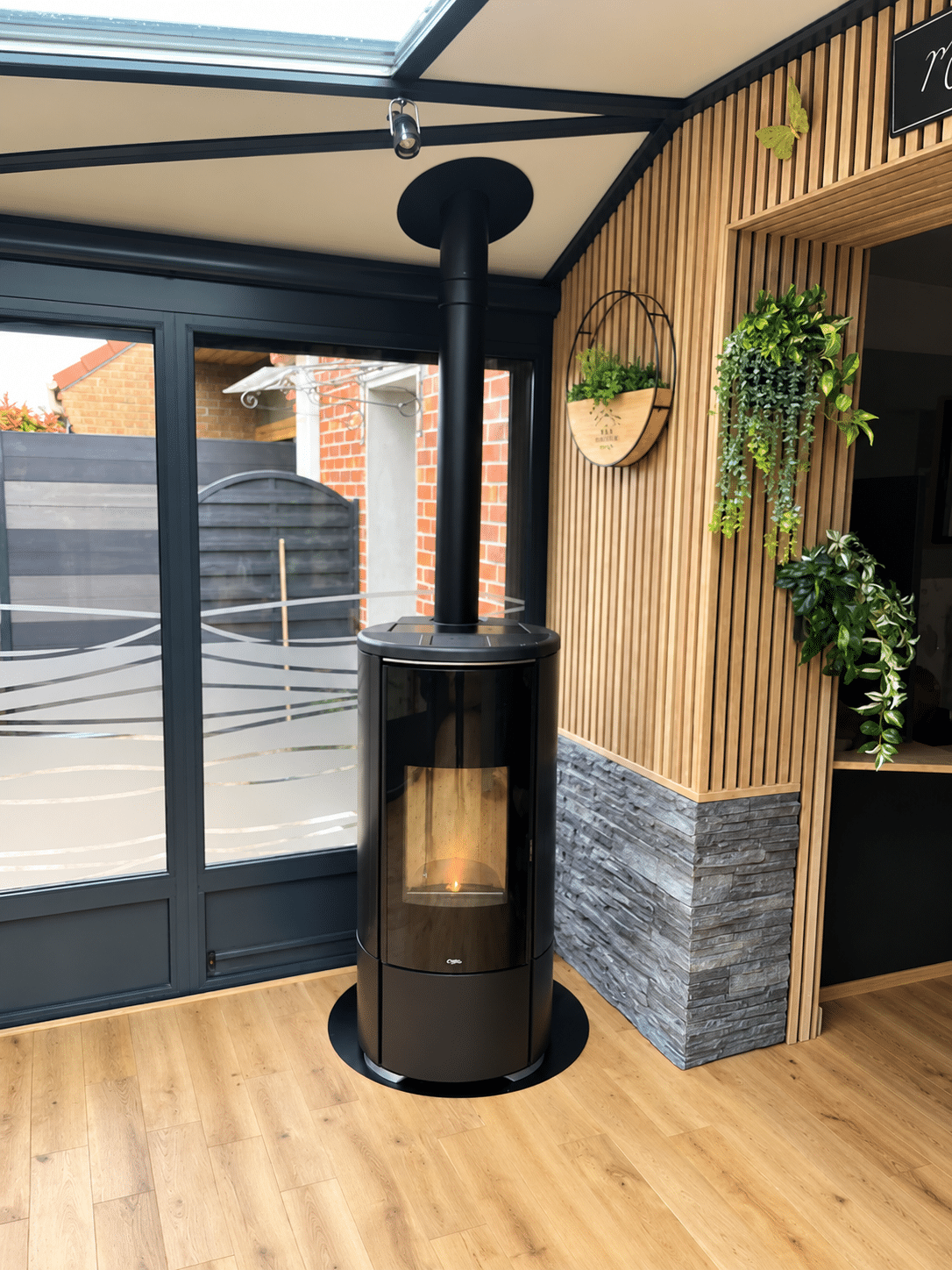 Poêle à Bois Moderne : Design Scandinave et Confort Poêle à bois noir moderne avec flamme, mur en tasseaux de bois et parement de pierre dans un intérieur élégant.
